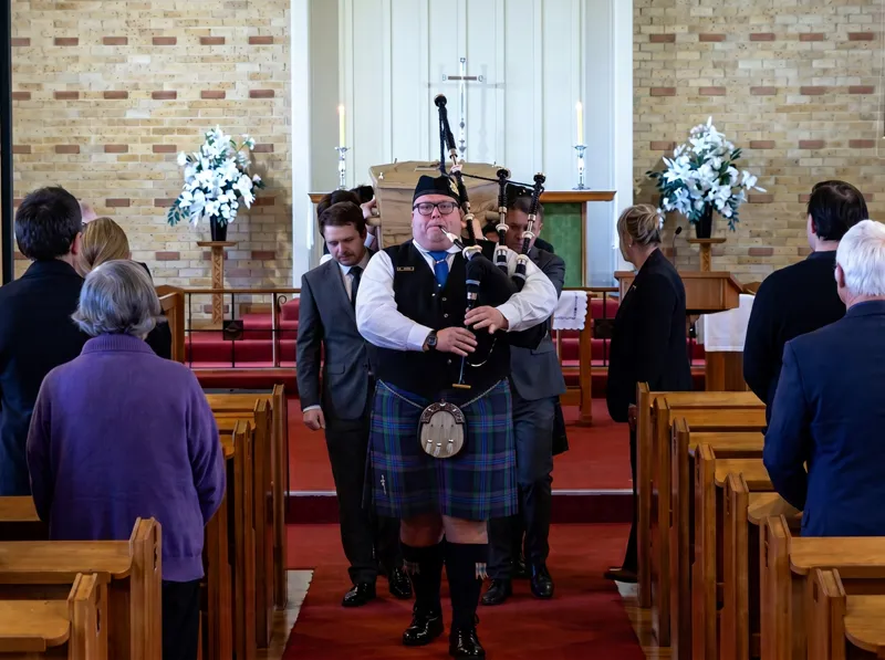 Damo the Piper leading a casket down the aisle at a chapel funeral service